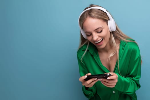 cute joyful attractive blonde young woman with headphones and smartphone on blue background.