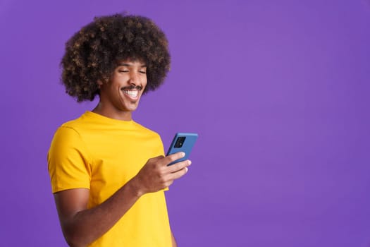 Happy african man with curly hair smiling while using a mobile in studio