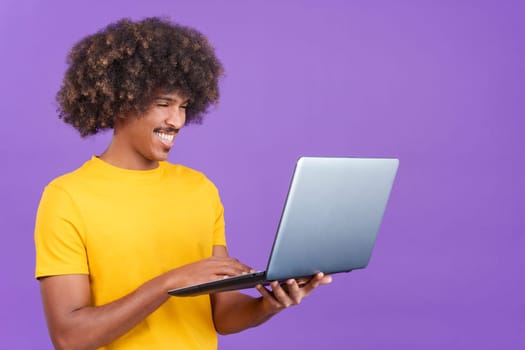 Happy african man wit curly hair standing and using a laptop in studio