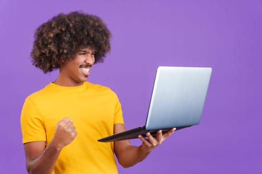 Happy african man with curly hair celebrating while using a laptop in studio