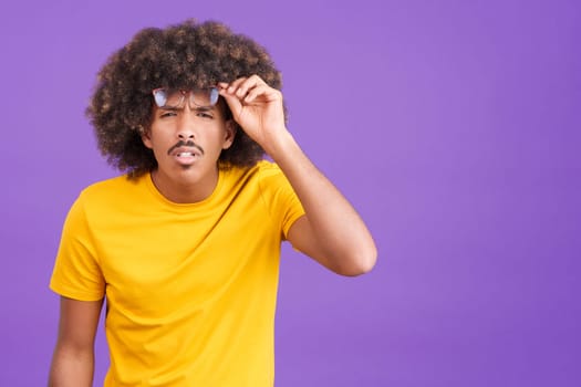 African man with curly hair taking off her glasses to see far away in studio