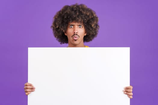 Surprised young african man with curly hair holding a blank panel in studio