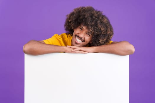 Cool african man with curly hair leaning on a blank panel in studio