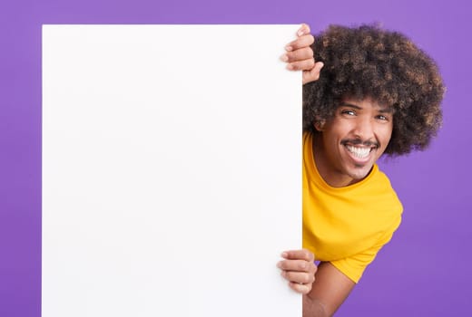 Smiley african man with curly hair holding a blank panel while looking at camera in studio