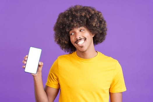 Smiley african man holding a mobile with a blank screen. Purple background