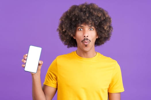 Surprised african man holding a mobile with a blank screen in studio