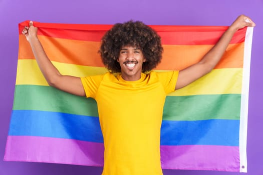 Happy african man raising a lgbt rainbow flag while looking at the camera in studio