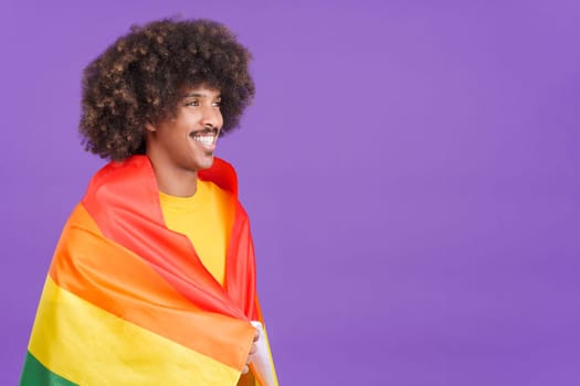 Smiling african man smiling at camera wrapped with a lgbt flag in studio