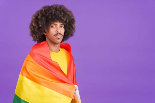Serious african man smiling at camera wrapped with a lgbt flag in studio