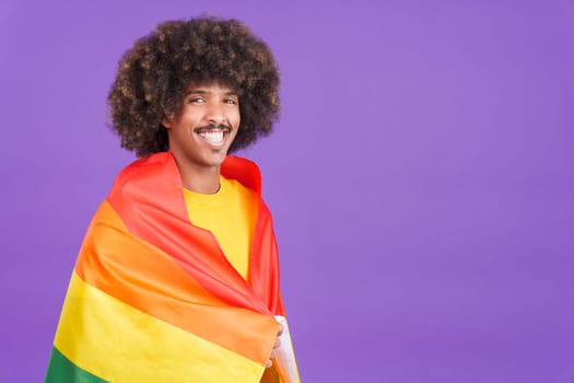 Happy african man smiling at camera wrapped with a lgbt flag in studio