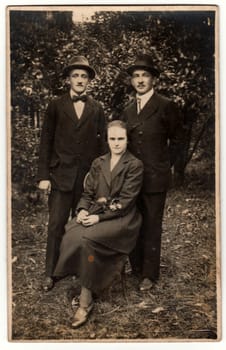 USTI NAD ORLICI, THE CZECHOSLOVAK REPUBLIC - CIRCA 1930s: Vintage photo shows two men and woman pose outside. Original retro black and white photography.