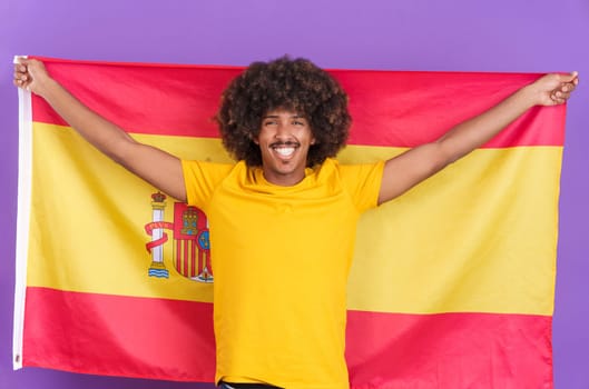 Happy african man with curly hair raising a spanish national flag in studio