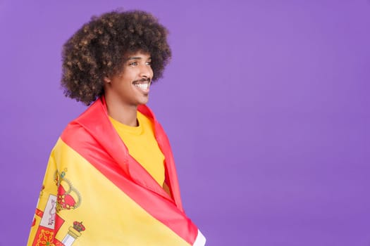 African man smiling while looking aside and wrapping with a spanish flag in studio