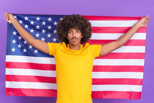 Serious african man raising a north america national flag while looking at the camera in studio