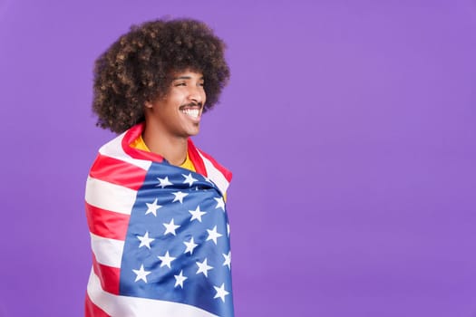 Dreamy african man with curly hair wrapping with a north america national flag in studio