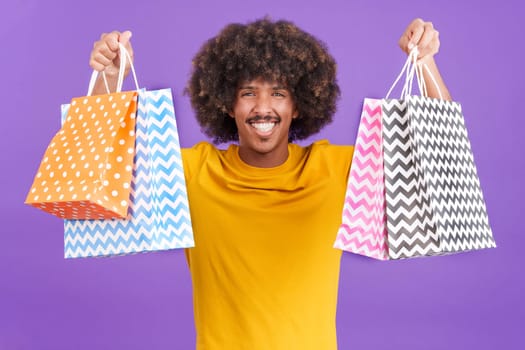 Happy african man smiling at the camera while showing shopping bags in studio