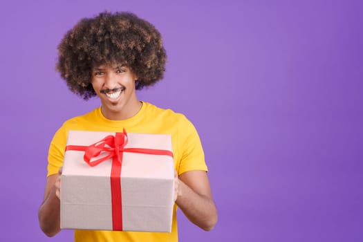 Happy african man smiling at camera while giving a gift with a red ribbon in studio