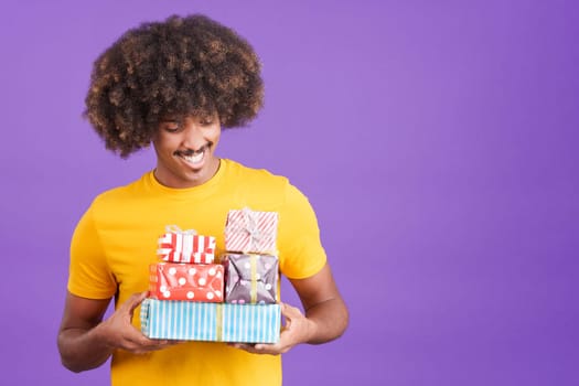 Stylish african man with curly hair smiling with many gifts in the hands in studio