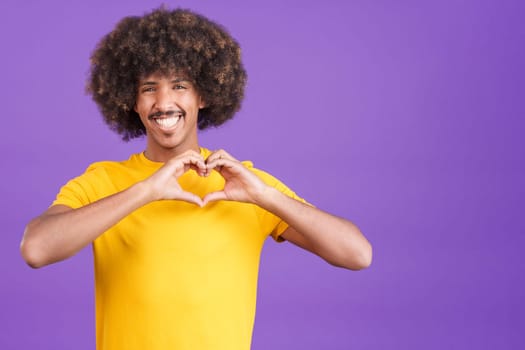 Happy african man with curly hair representing a heart in the shape of fingers in studio