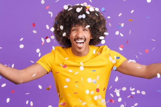 Cool african man with curly hair surrounded by multicolored confetti flying in the air in studio