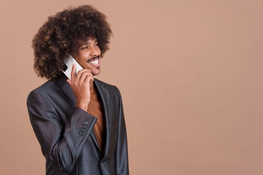 African elegant man with curly hair and black jacket talking to the mobile phone in studio