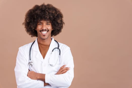 Smiley african doctor with curly hair looking at the camera with arms crossed in studio