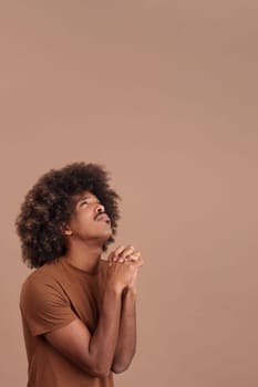 African man with curly hair looking up while praying with folded hands in studio