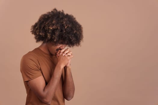 African man with curly hair praying with folded hands and closed eyes in studio