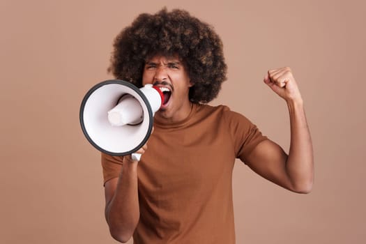 Upset african man with curly hair shouting using a loudspeaker in studio