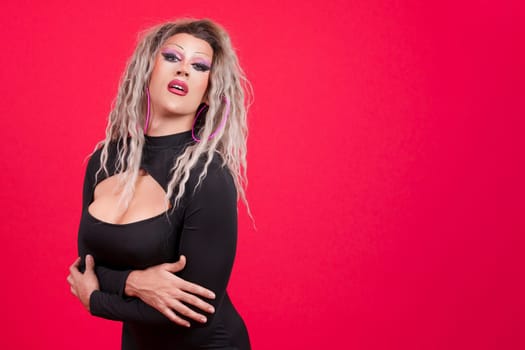 Sexy transgender person with make up looking at the camera in studio with red background