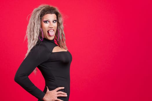 Playful transgender person dressed as drag queen sticking out his tongue in studio with red background