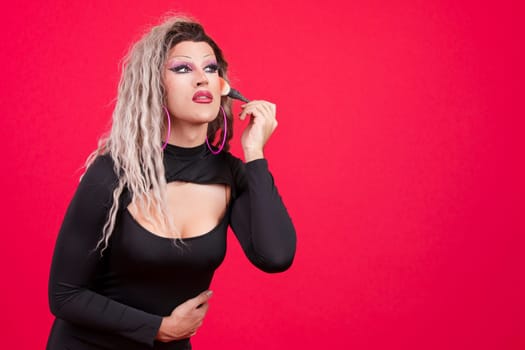 Transgender person dressed as drag queen making up in studio with red background