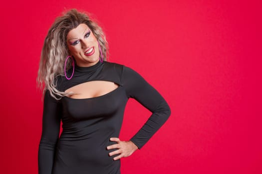Happy drag queen man posing while looking at the camera in studio with red background