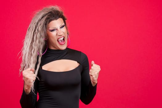 Passionate transgender person with make up celebrating raising the fist in studio with red background
