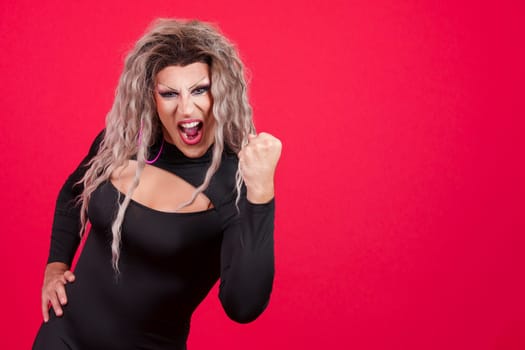Emotional transgender person with make up celebrating raising the fist in studio with red background