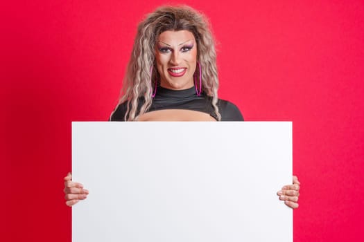 Smiley transgender person with make up holding a blank panel in studio with red background