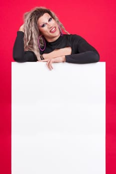 Transgender person with make up leaning on a blank panel in studio with red background