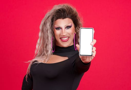Transgender person dressed as drag queen showing the blank screen of a mobile in a studio with red background