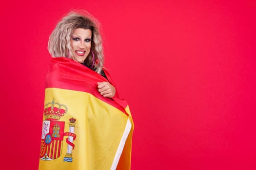 Smiley transgender person dressed as drag queen wrapping with a spanish flag in studio with red background