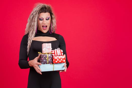 Surprised transgender person with make up holding many gifts in studio with red background