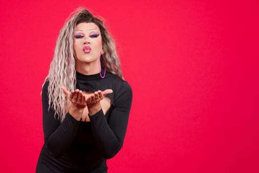 Transgender person dressed as drag queen blowing a kiss looking at camera in studio with red background
