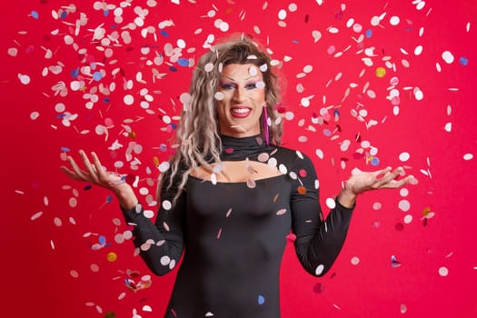 Drag queen person surrounded by confetti flying in the air in studio with red background