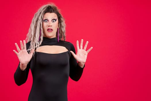 Surprised transgender person gesturing with the hands in fear in studio with red background