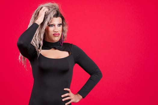 Drag queen man gesturing with doubtful expression in studio with a red background