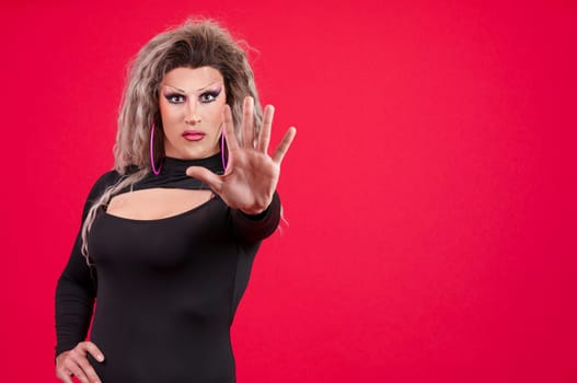 Transgender person gesturing prohibition with the palm of the hand in studio with red background