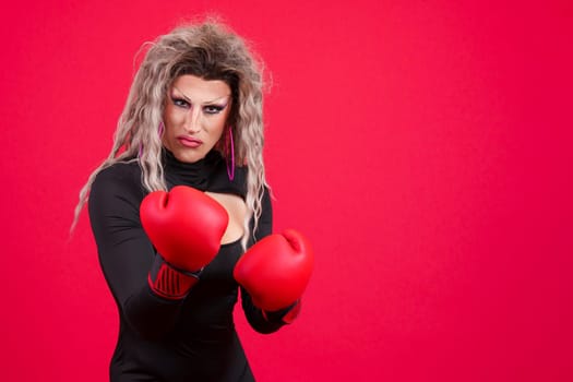 Transgender person with boxing gloves and agressive pose in studio in red background