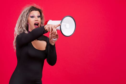 Transgender person pointing while using a loudspeaker in studio with a red background