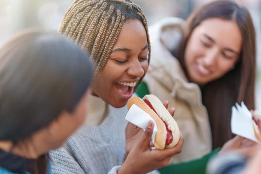 Happy african woman eating a hot dog next to friends in a park