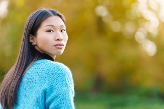 Serious asian woman turning to smile at the camera in a park