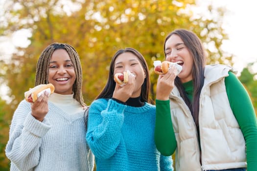 Low angle view of a group of multiethnic friends joking while eating hot dog in a park